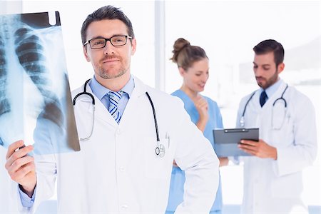 simsearch:400-07778150,k - Male doctor examining xray with colleagues in the background at medical office Stock Photo - Budget Royalty-Free & Subscription, Code: 400-07275996