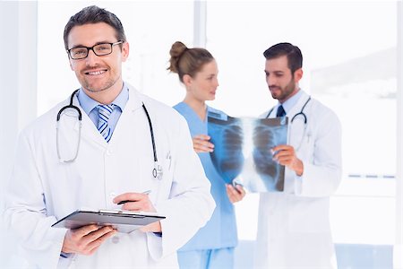 simsearch:400-07778150,k - Portrait of a male doctor holding reports with colleagues examining xray behind at medical office Stock Photo - Budget Royalty-Free & Subscription, Code: 400-07275997