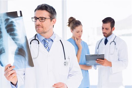 simsearch:400-07778150,k - Male doctor examining xray with colleagues in the background at medical office Stock Photo - Budget Royalty-Free & Subscription, Code: 400-07275993