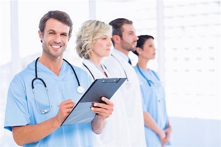 simsearch:614-06044418,k - Portrait of a male doctor writing reports with colleagues standing behind in a medical office Foto de stock - Super Valor sin royalties y Suscripción, Código: 400-07276037