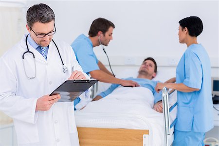 Doctor writing reports with patient and surgeons in background at the hospital Stock Photo - Budget Royalty-Free & Subscription, Code: 400-07276073