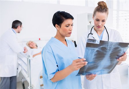 simsearch:400-07274751,k - Doctor and surgeon examining xray with patient in background at the hospital Foto de stock - Super Valor sin royalties y Suscripción, Código: 400-07276120