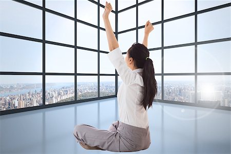 simsearch:400-07277816,k - Businesswoman sitting cross legged cheering against room with large windows showing city Fotografie stock - Microstock e Abbonamento, Codice: 400-07278332