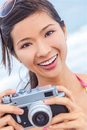 simsearch:400-08291180,k - A beautiful Asian Chinese girl or young woman wearing bikini at a beach looking happy taking pictures or photographs with a retro digital camera Foto de stock - Royalty-Free Super Valor e Assinatura, Número: 400-07272427