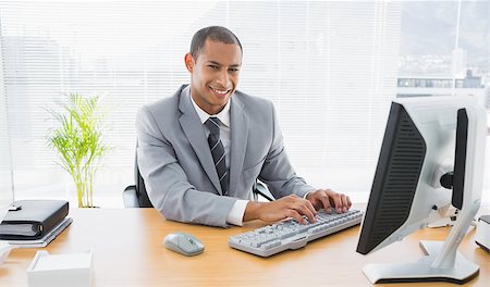 simsearch:400-07272682,k - Portrait of a smiling young businessman using computer at office desk Stockbilder - Microstock & Abonnement, Bildnummer: 400-07272685