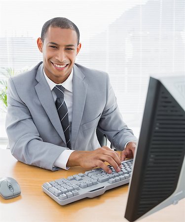 simsearch:400-07272682,k - Portrait of a smiling young businessman using computer at office desk Stockbilder - Microstock & Abonnement, Bildnummer: 400-07272686