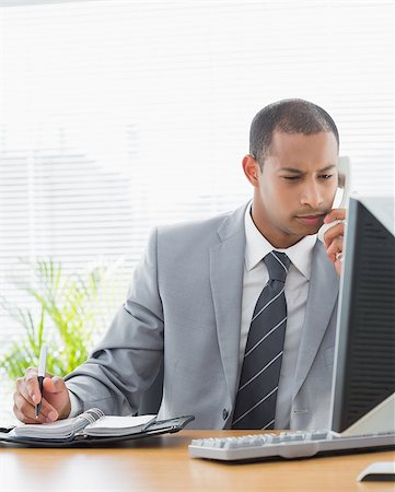 simsearch:400-07057750,k - Concentrated young businessman using computer and phone at office desk Photographie de stock - Aubaine LD & Abonnement, Code: 400-07272694