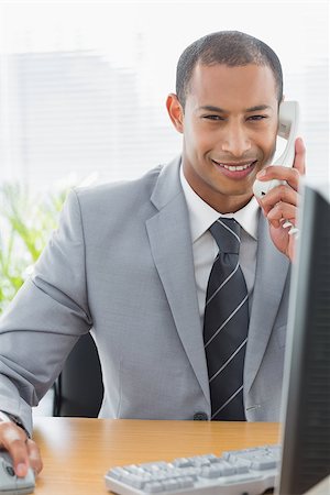 simsearch:400-07272682,k - Portrait of a smiling young businessman using computer and phone at office desk Stockbilder - Microstock & Abonnement, Bildnummer: 400-07272690