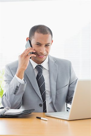 simsearch:400-07272682,k - Portrait of a smiling young businessman using laptop and cellphone at office desk Stockbilder - Microstock & Abonnement, Bildnummer: 400-07272700