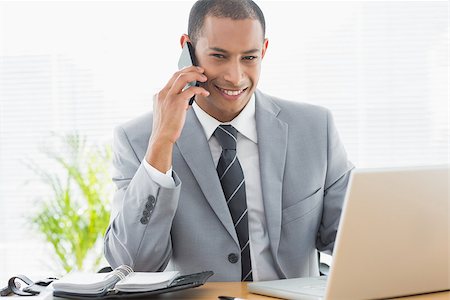 simsearch:400-07272682,k - Portrait of a smiling young businessman using laptop and cellphone at office desk Stockbilder - Microstock & Abonnement, Bildnummer: 400-07272701