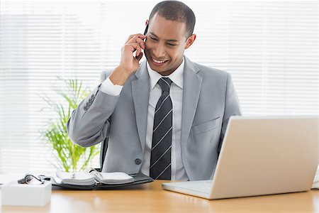 simsearch:400-07927298,k - Smiling young businessman with laptop using cellphone at office desk Foto de stock - Royalty-Free Super Valor e Assinatura, Número: 400-07272718
