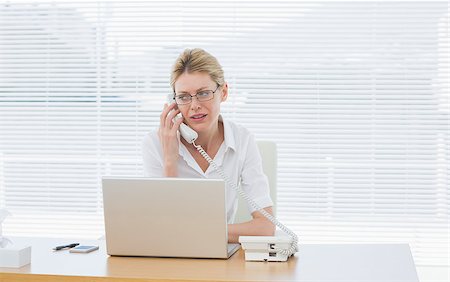 simsearch:400-05663929,k - Concentrated young businesswoman using laptop and phone at office desk Stock Photo - Budget Royalty-Free & Subscription, Code: 400-07272783