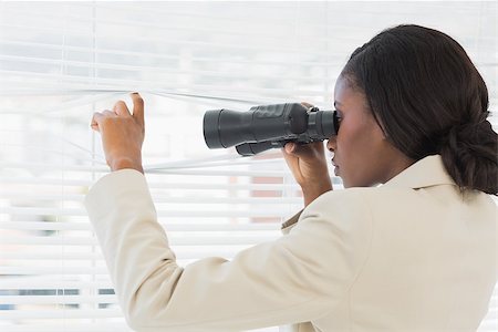 Side view of a serious businesswoman peeking with binoculars through blinds in the office Foto de stock - Super Valor sin royalties y Suscripción, Código: 400-07272839