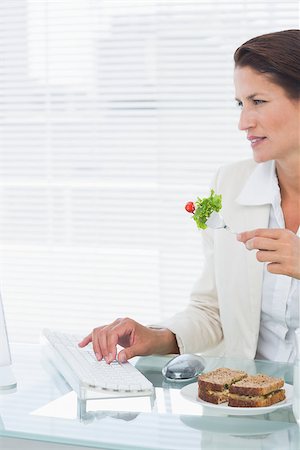 simsearch:400-07272682,k - Concentrated young businesswoman using computer while eating salad at office desk Stockbilder - Microstock & Abonnement, Bildnummer: 400-07272847