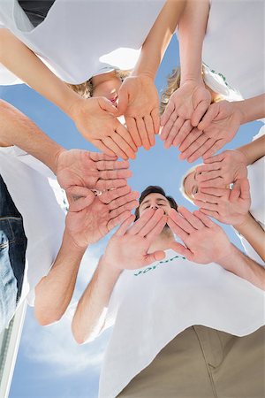 simsearch:400-07273325,k - Low angle view of happy volunteers with hands together against blue sky Foto de stock - Royalty-Free Super Valor e Assinatura, Número: 400-07273319