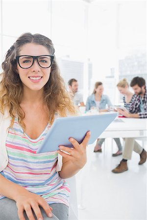 simsearch:400-07273325,k - Smiling young woman using digital tablet with colleagues in background at a creative bright office Foto de stock - Royalty-Free Super Valor e Assinatura, Número: 400-07273456