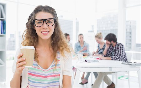 simsearch:400-07273325,k - Smiling young woman holding disposable coffee cup with colleagues in background at a creative bright office Foto de stock - Royalty-Free Super Valor e Assinatura, Número: 400-07273457