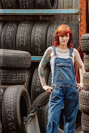 Photo of a young beautiful redhead mechanic wearing overalls and standing in an old garage. Attached property release is for arm tattoos. Stock Photo - Budget Royalty-Free & Subscription, Code: 400-07294062
