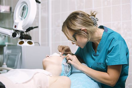simsearch:400-07952664,k - Young female beautician in a skin clinic with a patient preparing her for laser treatment fitting protective eye goggles and applying cream to the delicate skin around the eye Foto de stock - Super Valor sin royalties y Suscripción, Código: 400-07296554
