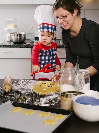 Photo of an adorable boy in a chef hat and apron and his mother making cookies in the kitchen. Stock Photo - Budget Royalty-Free & Subscription, Code: 400-07298234