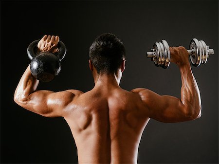 simsearch:400-06208099,k - Photo of an Asian male exercising with both a kettlebell and a dumbbell, doing shoulder press over dark background. Photographie de stock - Aubaine LD & Abonnement, Code: 400-07298240