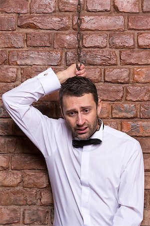 suicide by hanging - Conceptual image of a desperate handsome businessman in a bow tie standing against a brick wall with a chain around his neck and a disconsolate depressed expression Stock Photo - Budget Royalty-Free & Subscription, Code: 400-07301611