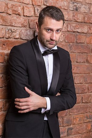 Elegant handsome macho man in a bow tie and tuxedo leaning against a brick wall giving the camera a sultry look Stock Photo - Budget Royalty-Free & Subscription, Code: 400-07301613