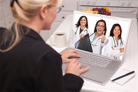 simsearch:400-06857713,k - Woman Sitting In Kitchen Using Laptop Viewing Team of Hispanic Female Doctors or Nurses with Thumbs Up Holding X-ray. Fotografie stock - Microstock e Abbonamento, Codice: 400-07303423