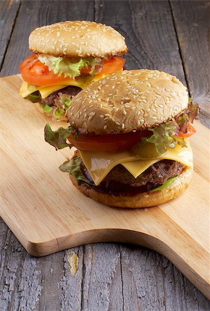 simsearch:400-06330800,k - Two Tasty Hamburgers with Beef, Tomato, Lettuce, Pickle, Red Onion and Cheese into Sesame Buns closeup on Wooden Cutting Board Stock Photo - Budget Royalty-Free & Subscription, Code: 400-07317003