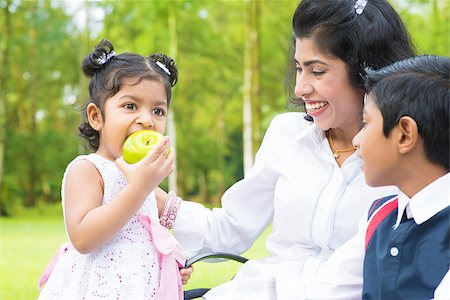 Happy Indian family. Asian girl eating an green apple at outdoor with mother and sibling. Stock Photo - Budget Royalty-Free & Subscription, Code: 400-07318226
