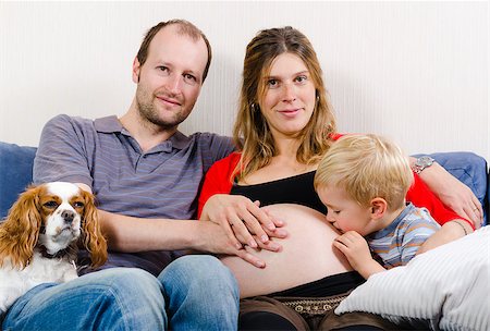 Happy young family sitting on the blue sofa expecting new baby Fotografie stock - Microstock e Abbonamento, Codice: 400-07311857
