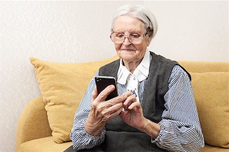 Senior woman using mobile phone while sitting on sofa Foto de stock - Super Valor sin royalties y Suscripción, Código: 400-07320902