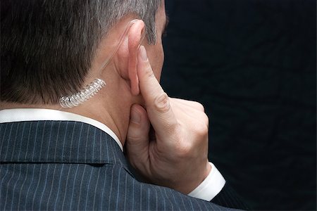 Close-up of a secret service agent listening to his earpiece, over the shoulder. Stock Photo - Budget Royalty-Free & Subscription, Code: 400-07321224