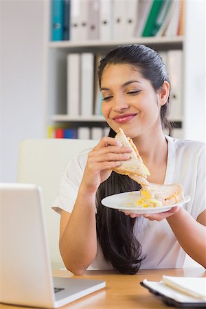 Young businesswoman having sandwich while looking at laptop in office Foto de stock - Super Valor sin royalties y Suscripción, Código: 400-07334205