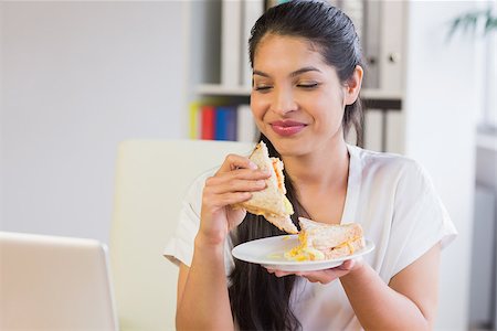 Young smiling businesswoman eating sandwich in lunch break at office Foto de stock - Super Valor sin royalties y Suscripción, Código: 400-07334206