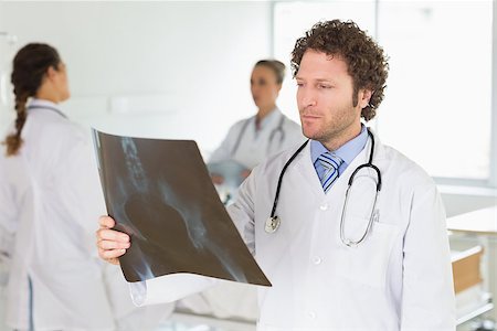 simsearch:400-07778150,k - Male doctor checking Xray with colleagues in background at hospital Stock Photo - Budget Royalty-Free & Subscription, Code: 400-07334488