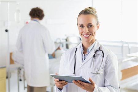 photo of patient in hospital in usa - Portrait of smiling female doctor using digital tablet with colleague examining patient in background at hospital Stock Photo - Budget Royalty-Free & Subscription, Code: 400-07334493