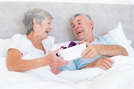 simsearch:400-07334704,k - Happy senior couple holding gift box while relaxing in bed at home Stock Photo - Budget Royalty-Free & Subscription, Code: 400-07334661