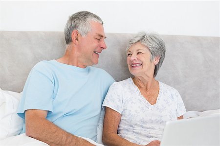 simsearch:400-07334704,k - Happy senior couple with laptop looking at each other in bed at home Stock Photo - Budget Royalty-Free & Subscription, Code: 400-07334689