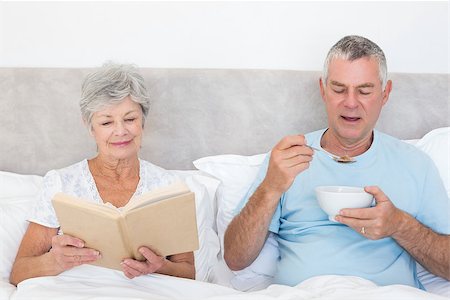 simsearch:400-07334704,k - Senior woman reading book while man having cereals in bed at home Stock Photo - Budget Royalty-Free & Subscription, Code: 400-07334681
