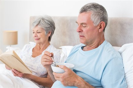 simsearch:400-07334704,k - Senior man eating cereals while wife reading book in bed at home Stock Photo - Budget Royalty-Free & Subscription, Code: 400-07334682