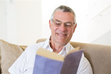 simsearch:400-04026722,k - Smiling senior man reading book while sitting on sofa at home Stock Photo - Budget Royalty-Free & Subscription, Code: 400-07334716