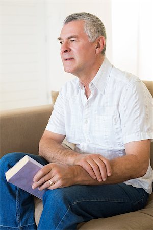 simsearch:400-04026722,k - Thoughtful senior man holding book while sitting on sofa at home Stock Photo - Budget Royalty-Free & Subscription, Code: 400-07334719