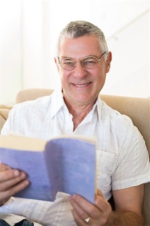 simsearch:400-04026722,k - Portrait of smiling senior man holding book while sitting on sofa at home Stock Photo - Budget Royalty-Free & Subscription, Code: 400-07334713