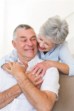 simsearch:400-04151970,k - Loving senior woman embracing husband sitting on sofa at home Fotografie stock - Microstock e Abbonamento, Codice: 400-07334738