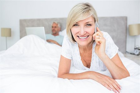 Portrait of a happy mature woman using cellphone while man using laptop in bed at home Stock Photo - Budget Royalty-Free & Subscription, Code: 400-07335221