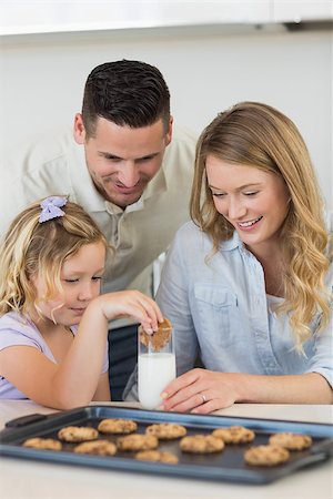 Father and mother looking at daughter dipping cookie in glass of milk Stock Photo - Budget Royalty-Free & Subscription, Code: 400-07335575