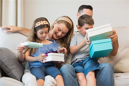 Happy family opening gifts while sitting on sofa at home Stock Photo - Budget Royalty-Free & Subscription, Code: 400-07335606