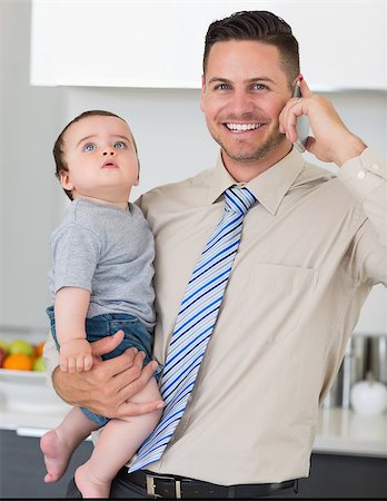 Portrait of handsome businessman using cellphone while carrying baby boy in house Stock Photo - Budget Royalty-Free & Subscription, Code: 400-07335639