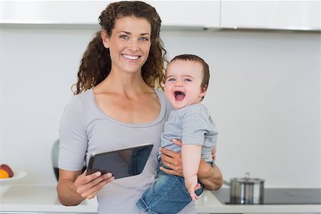 simsearch:400-08835171,k - Portrait of happy mother carrying cheerful baby boy while holding digital tablet in kitchen at home Photographie de stock - Aubaine LD & Abonnement, Code: 400-07335657